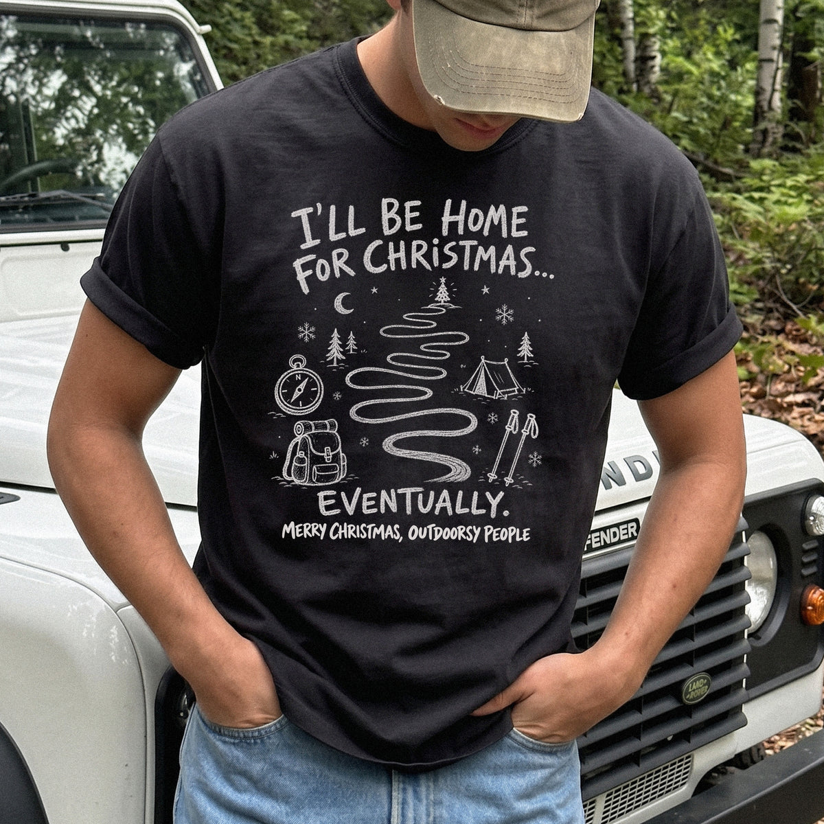 Man wearing a Black T-shirt printed with a winding trail with a tent, compass, backpack, trekking poles, snowflakes, and pine trees, doodle style