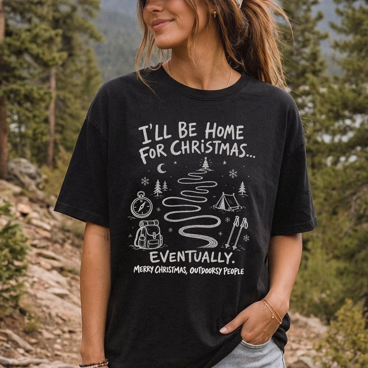 Woman wearing a Black T-shirt printed with a winding trail with a tent, compass, backpack, trekking poles, snowflakes, and pine trees, doodle style
