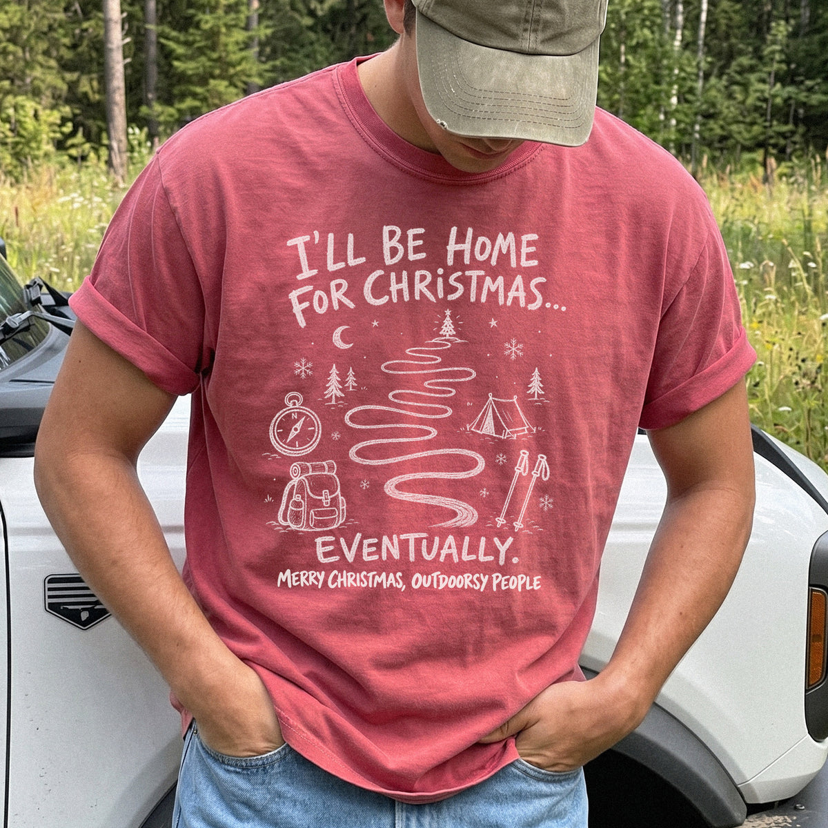 Man wearing a Crimson T-shirt printed with a winding trail with a tent, compass, backpack, trekking poles, snowflakes, and pine trees, doodle style