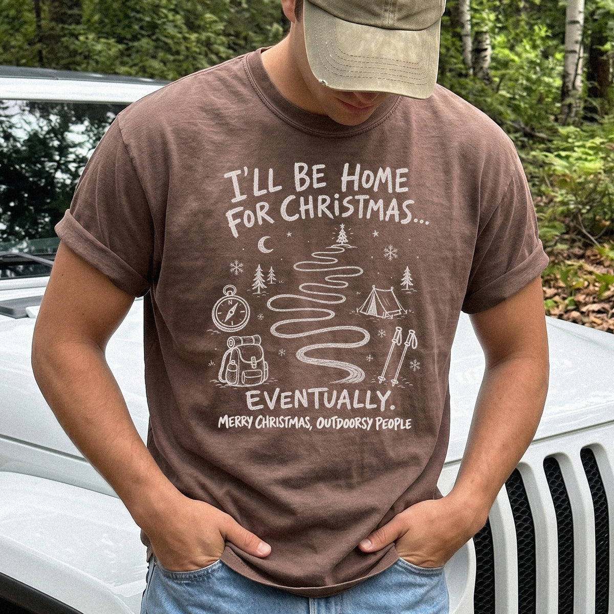 Man wearing an Espresso T-shirt printed with a winding trail with a tent, compass, backpack, trekking poles, snowflakes, and pine trees, doodle style