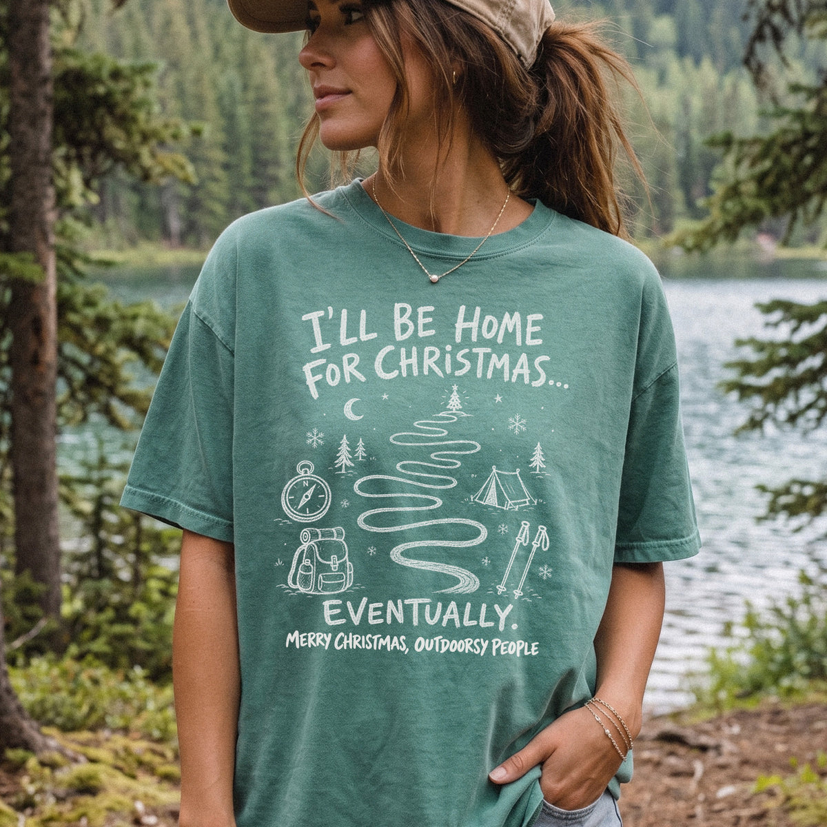 Woman wearing a Light Green T-shirt printed with a winding trail with a tent, compass, backpack, trekking poles, snowflakes, and pine trees, doodle style