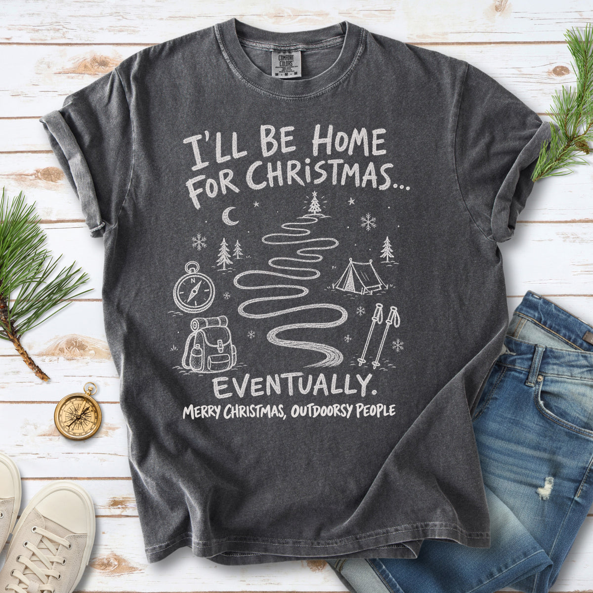A winding trail with a tent, compass, backpack, trekking poles, snowflakes, and pine trees, doodle style design on a Pepper T-shirt