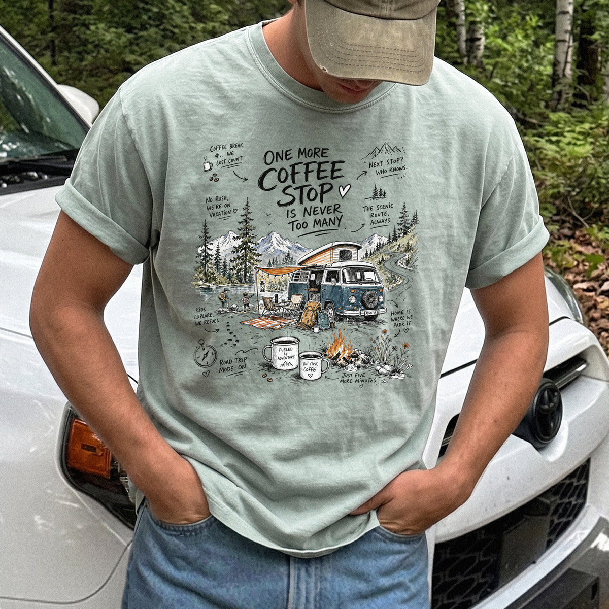Man wearing a Bay Comfort Colors T-shirt with a retro camper van parked by the water with mountain views and camp chairs