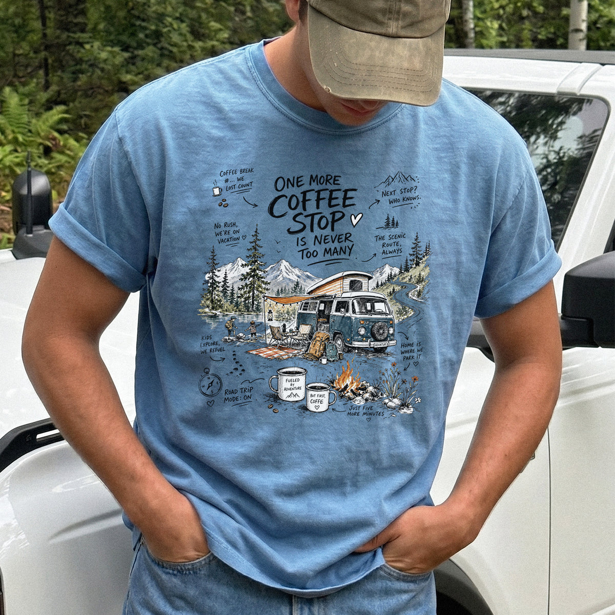 Man wearing a Blue Jean Comfort Colors T-shirt with a retro camper van parked by the water with mountain views and camp chairs