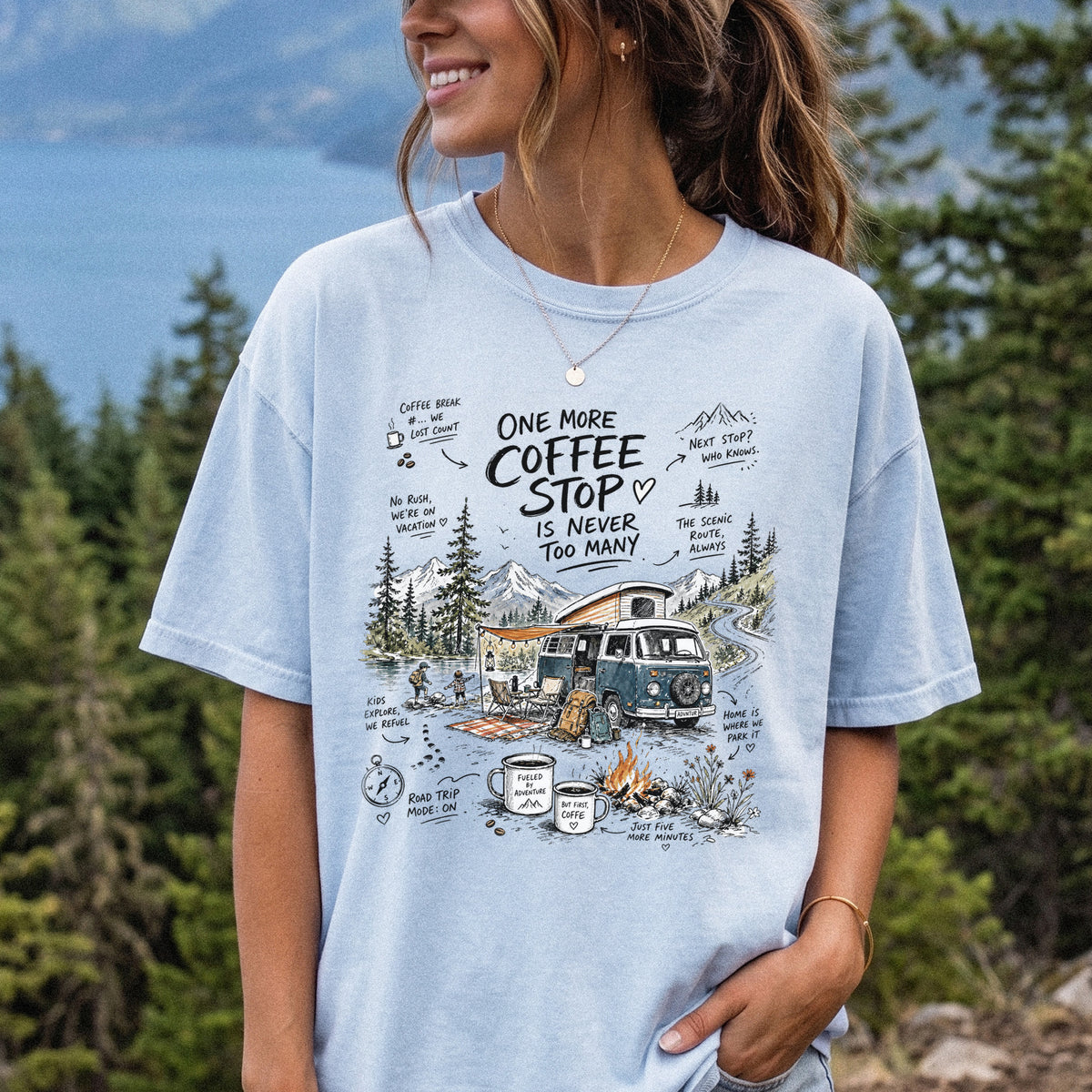 Woman wearing a Chambray Comfort Colors T-shirt printed with a retro camper van parked by the water with mountain views and camp chairs