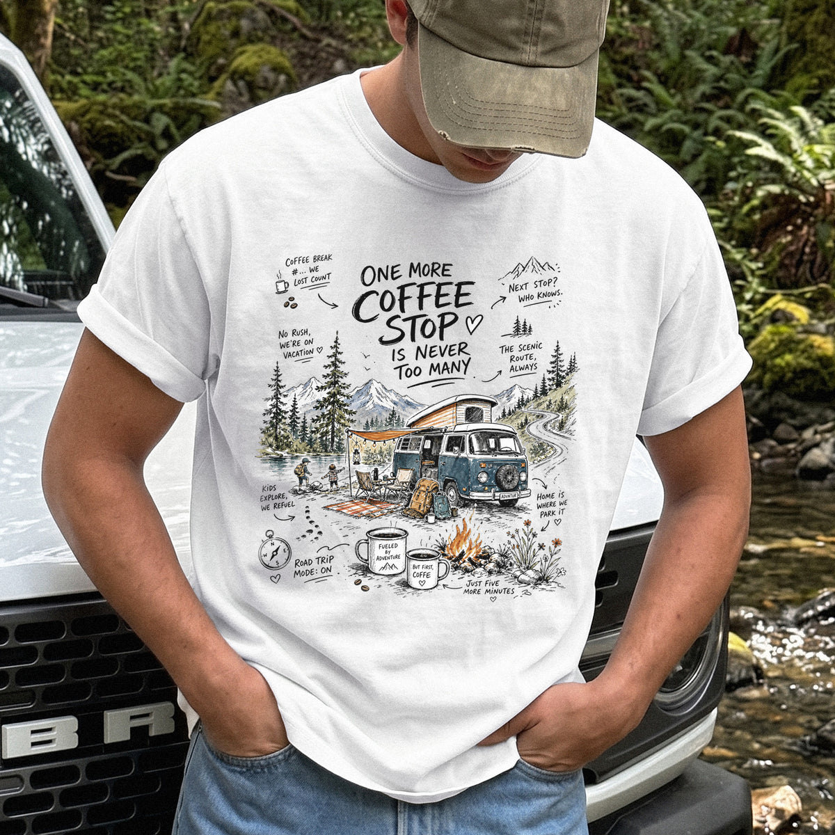 Man wearing a White Comfort Colors T-shirt with a retro camper van parked by the water with mountain views and camp chairs