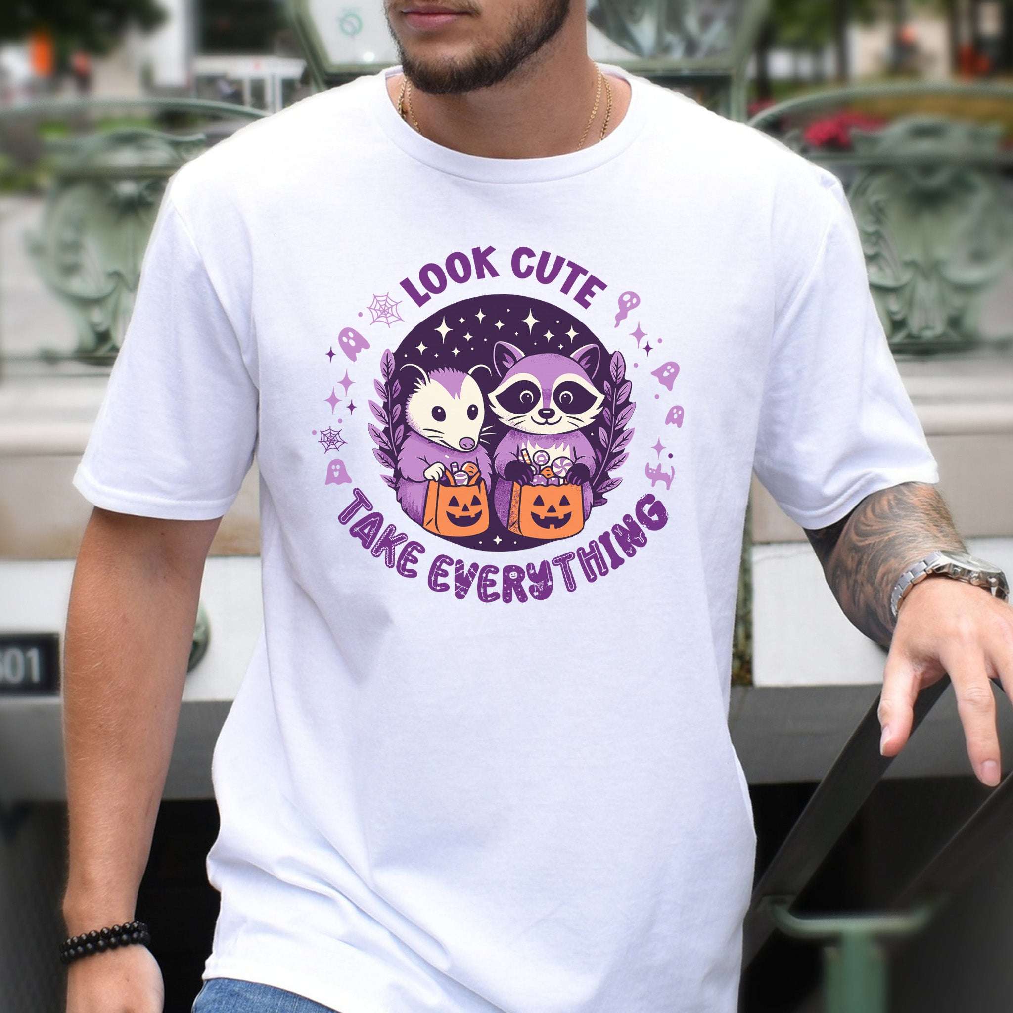 Opossum & raccoon Halloween T-shirt design featuring 'Look Cute, Take Everything' motto with pastel colors.