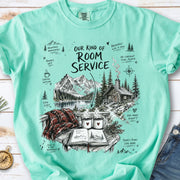 A cozy lakeside cabin scene with Rocky Mountain peaks, coffee mugs, and a journal design on an Island Reef Comfort Colors T-shirt
