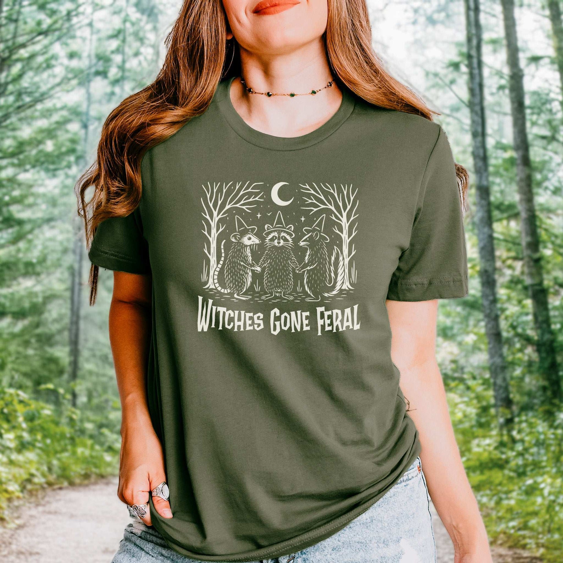 Witches Gone Feral Halloween T-shirt featuring raccoon, opossum, and skunk in a magical forest setting.