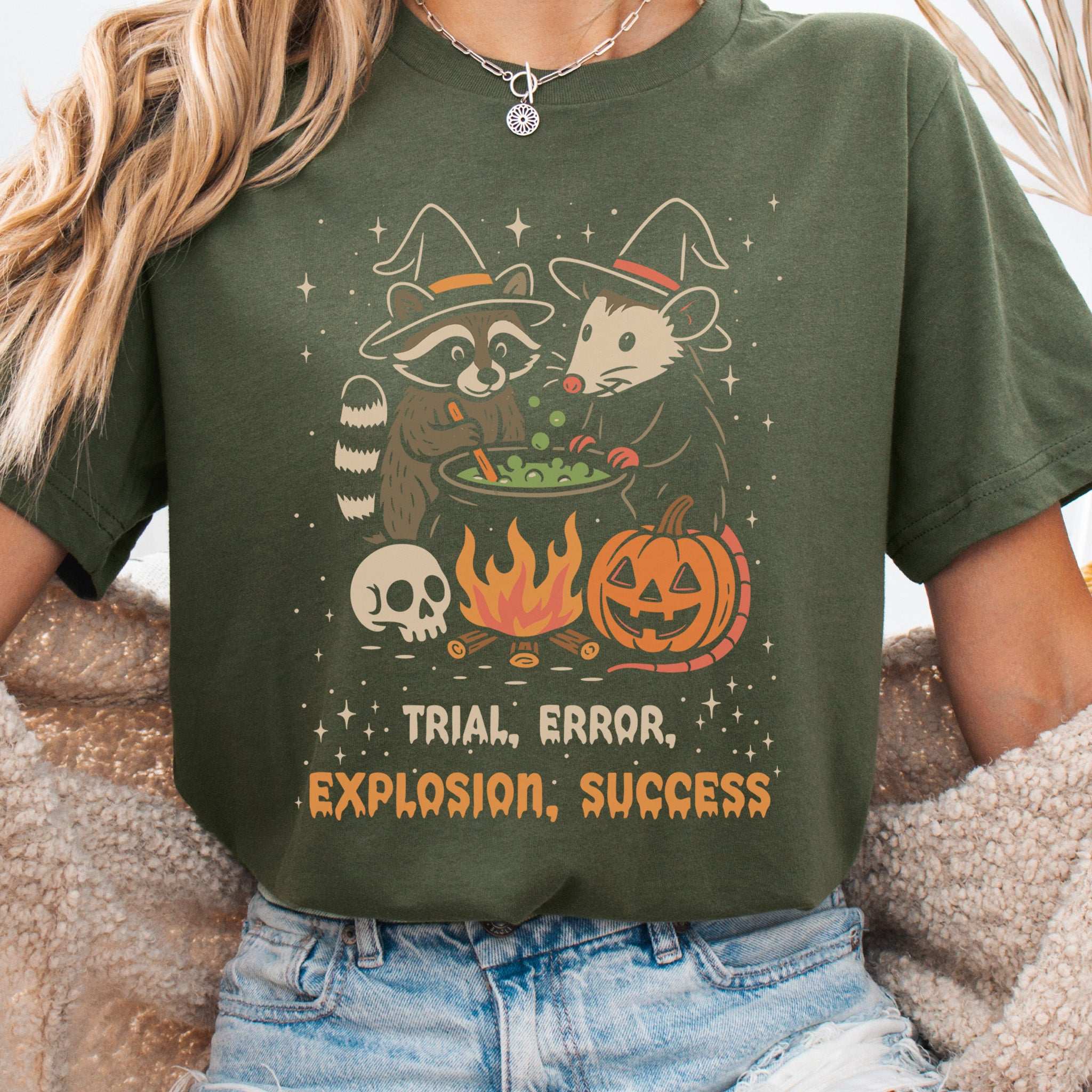 Potion Explosion Halloween T-shirt featuring a raccoon and opossum in a witch lab with the text 'Trial, Error, Explosion, Success'.