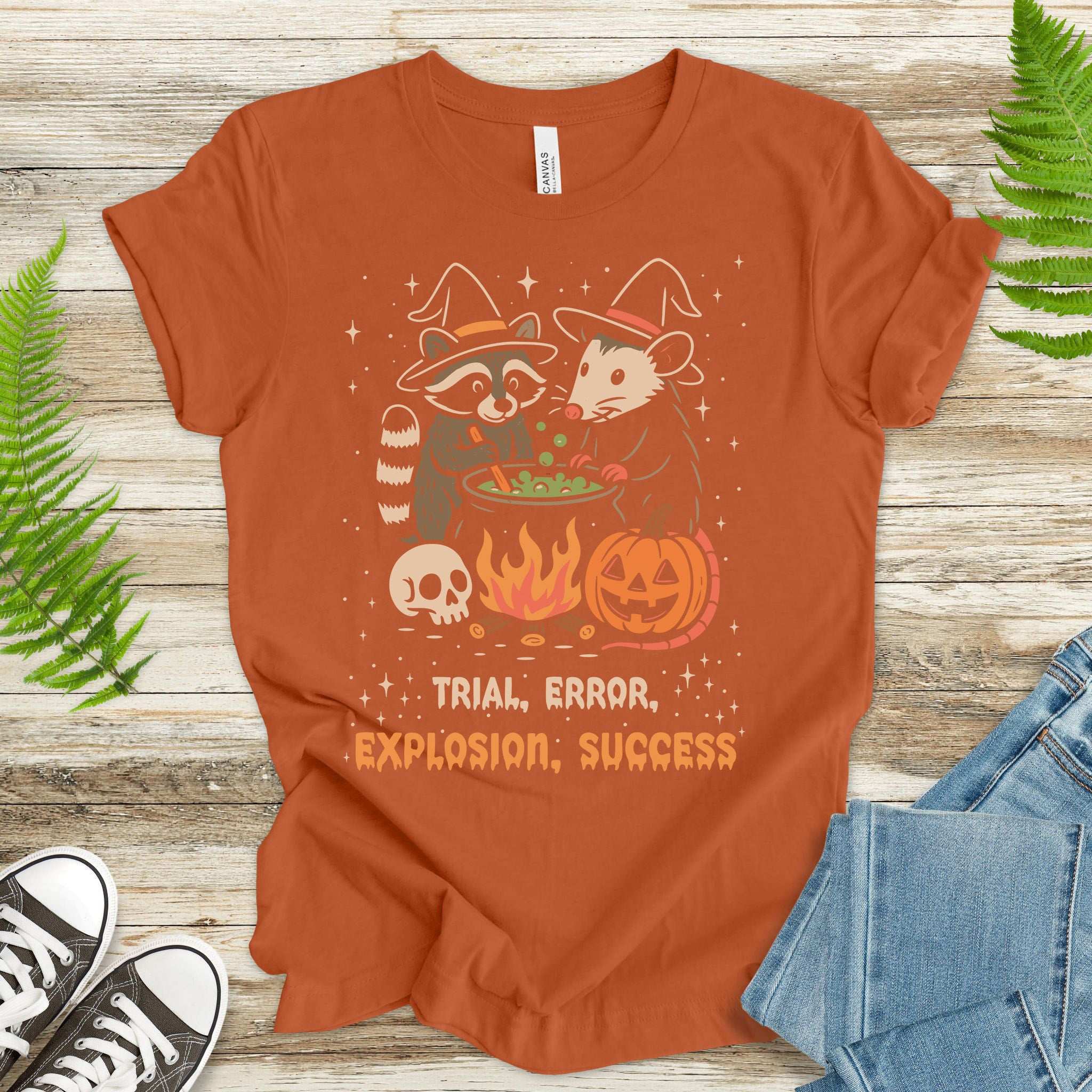 Potion Explosion Halloween T-shirt featuring a raccoon and opossum in witch hats brewing a magical potion.