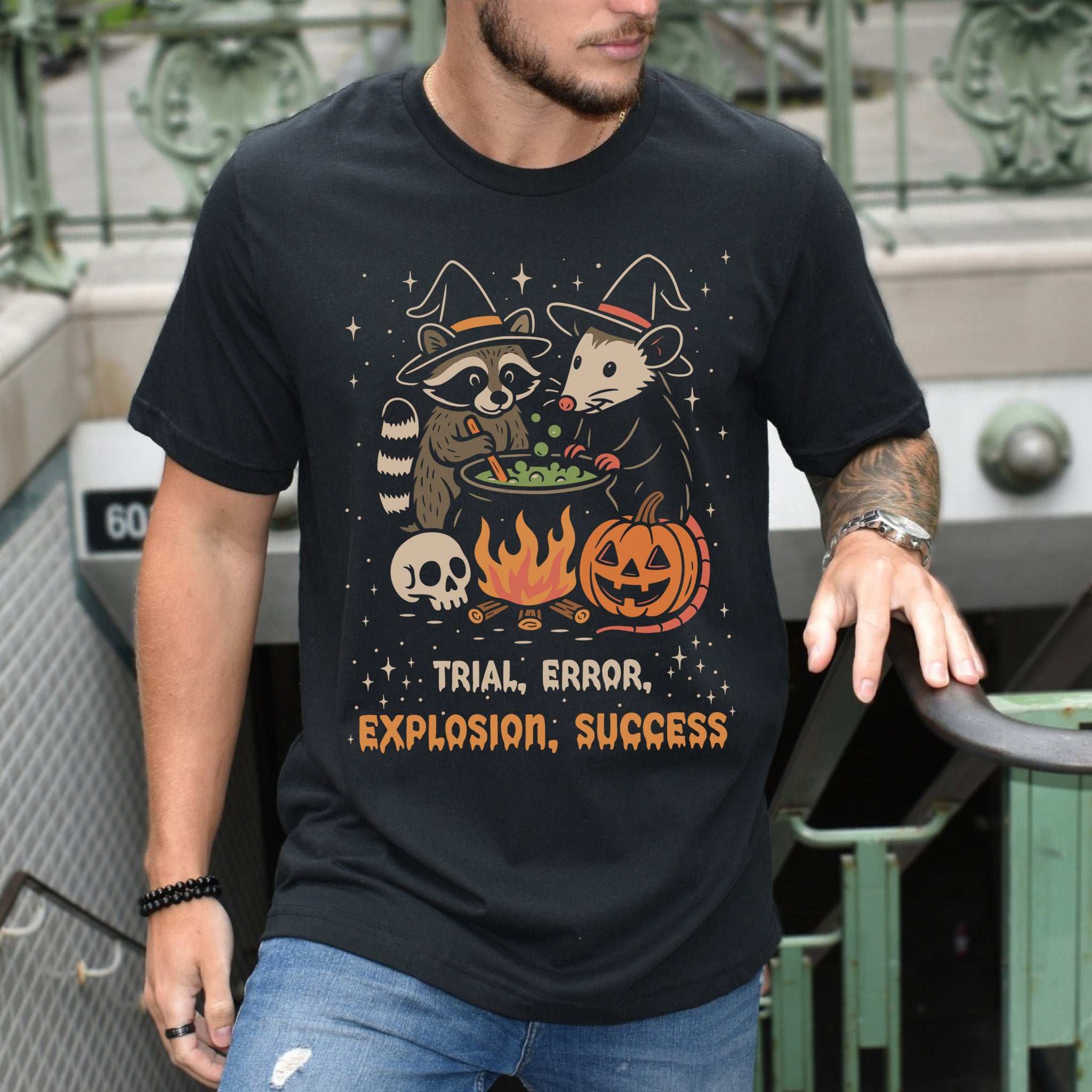 Potion Explosion Halloween T-shirt featuring a raccoon and opossum with cauldron, skull, and pumpkin design.