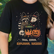 Potion Explosion Halloween T-shirt featuring raccoon and opossum witches in a cauldron with pumpkins.