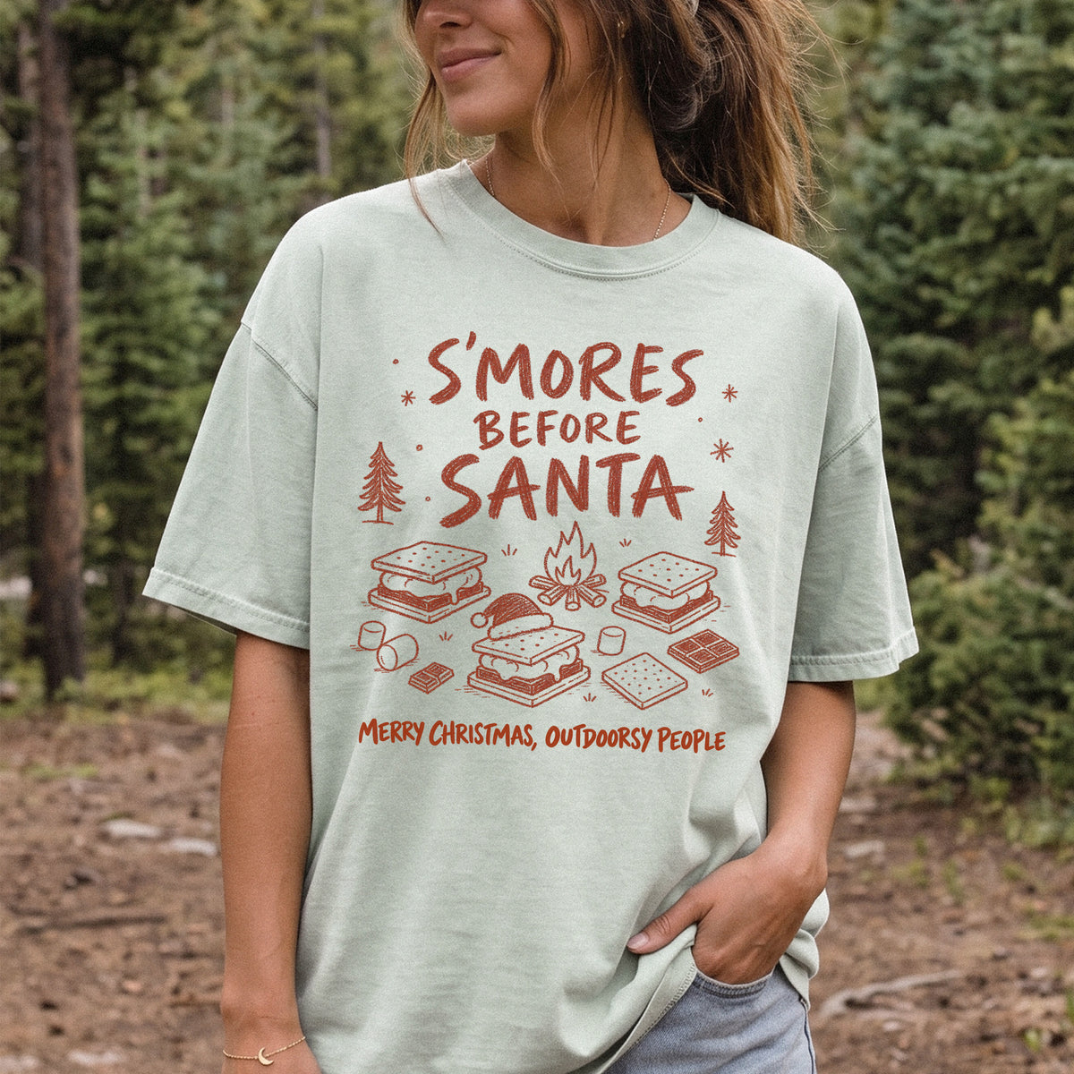 Woman wearing a Bay T-shirt printed with s’mores, a crackling campfire, marshmallows, chocolate pieces, pine trees, and a tiny Santa hat, doodle style
