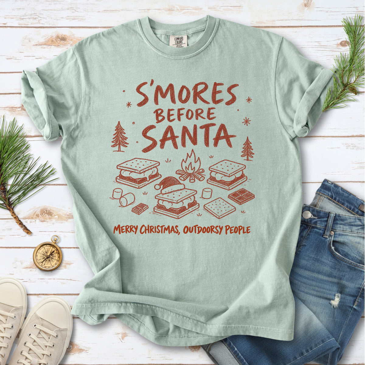 S’mores, a crackling campfire, marshmallows, chocolate pieces, pine trees, and a tiny Santa hat, doodle style design on a Bay T-shirt
