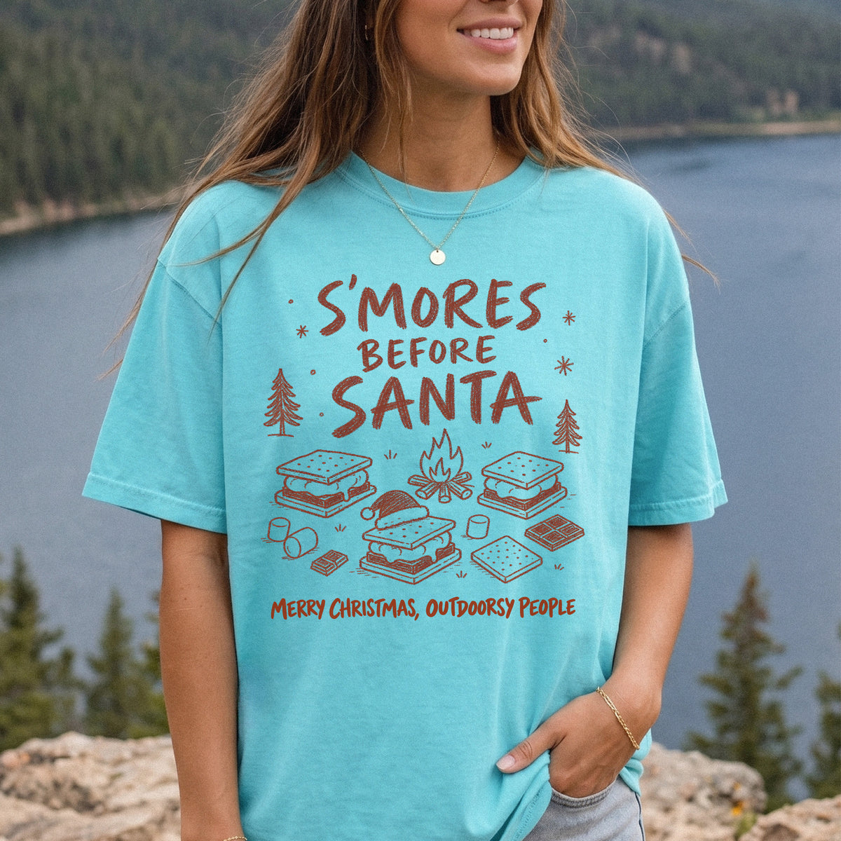 Woman wearing a Chalky Mint T-shirt printed with s’mores, a crackling campfire, marshmallows, chocolate pieces, pine trees, and a tiny Santa hat, doodle style