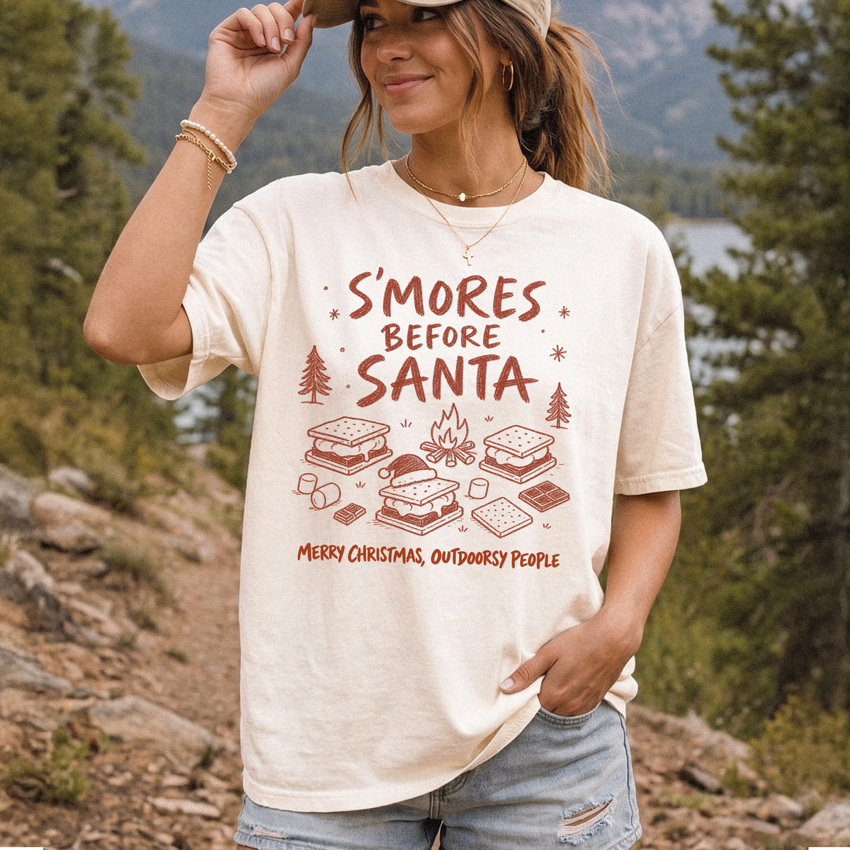 Woman wearing an Ivory T-shirt printed with s’mores, a crackling campfire, marshmallows, chocolate pieces, pine trees, and a tiny Santa hat, doodle style