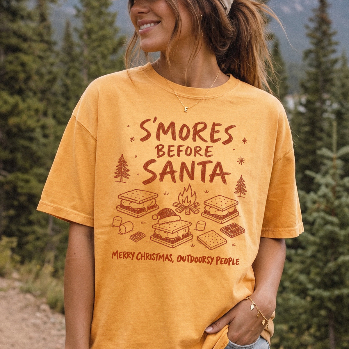 Woman wearing a Mustard T-shirt printed with s’mores, a crackling campfire, marshmallows, chocolate pieces, pine trees, and a tiny Santa hat, doodle style