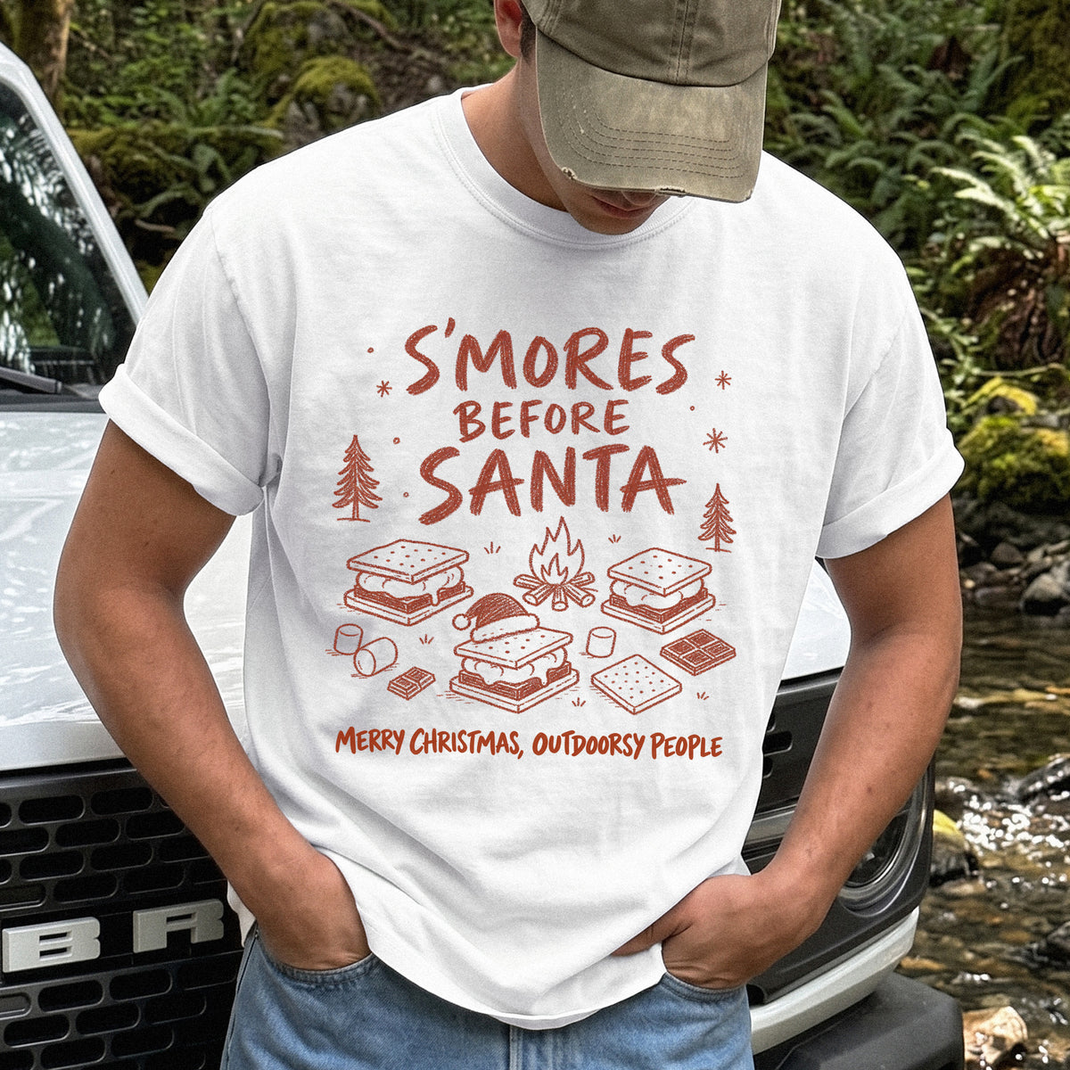 Man wearing a White T-shirt printed with s’mores, a crackling campfire, marshmallows, chocolate pieces, pine trees, and a tiny Santa hat, doodle style