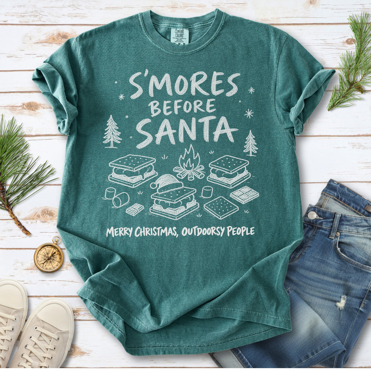 S’mores, a crackling campfire, marshmallows, chocolate pieces, pine trees, and a tiny Santa hat, doodle style design on a Blue Spruce T-shirt