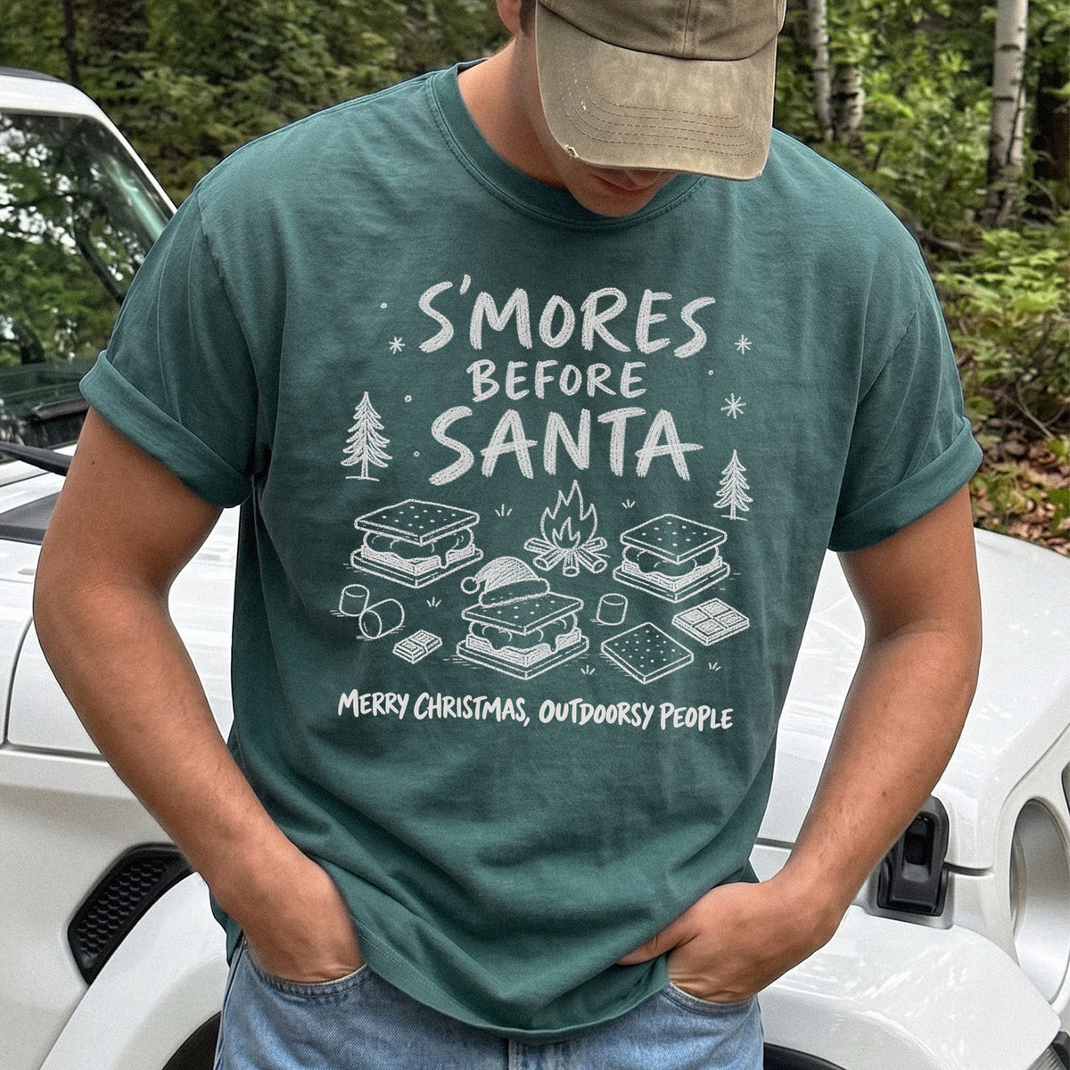 Man wearing a Blue Spruce T-shirt printed with s’mores, a crackling campfire, marshmallows, chocolate pieces, pine trees, and a tiny Santa hat, doodle style