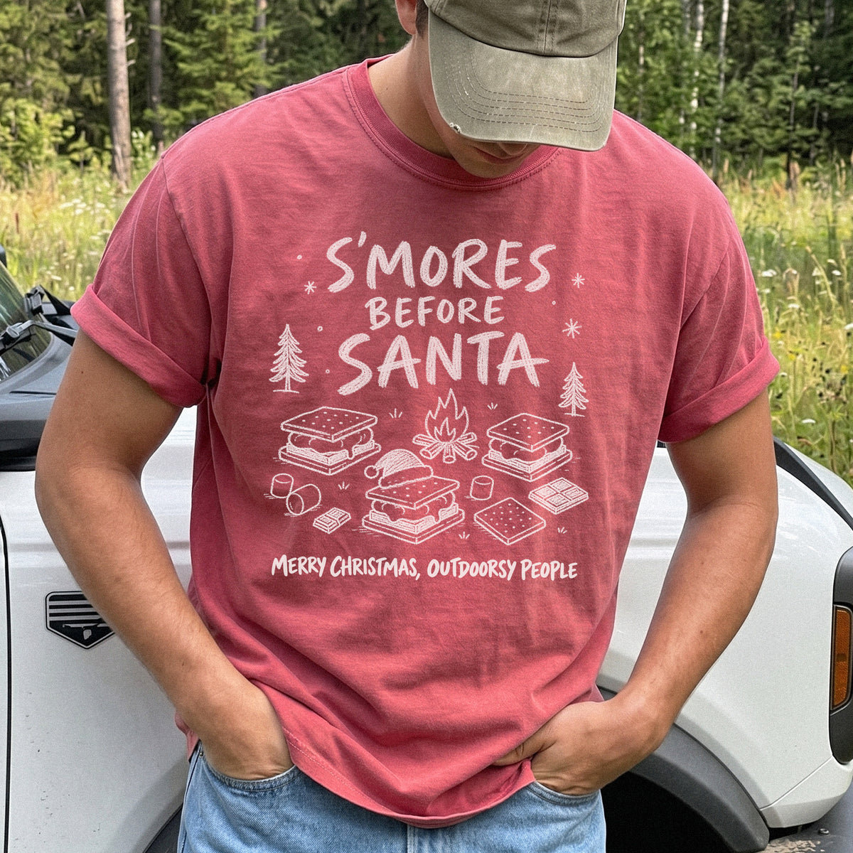 Man wearing a Crimson T-shirt printed with s’mores, a crackling campfire, marshmallows, chocolate pieces, pine trees, and a tiny Santa hat, doodle style