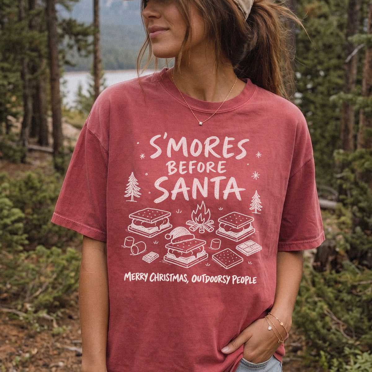 Woman wearing a Crimson T-shirt printed with s’mores, a crackling campfire, marshmallows, chocolate pieces, pine trees, and a tiny Santa hat, doodle style