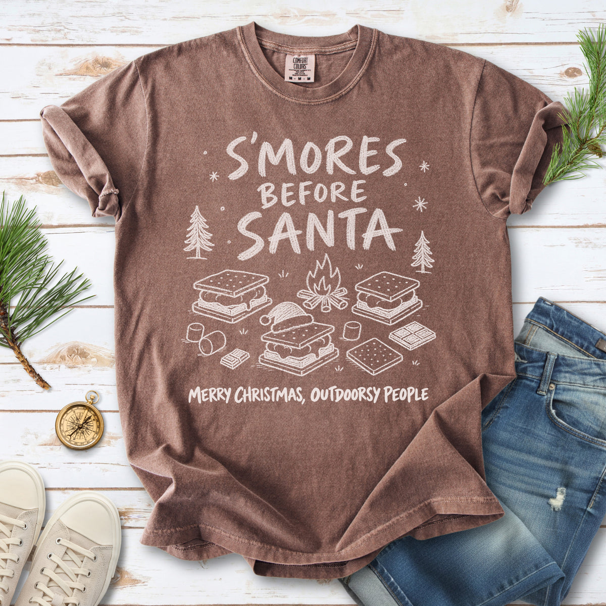 S’mores, a crackling campfire, marshmallows, chocolate pieces, pine trees, and a tiny Santa hat, doodle style design on an Espresso T-shirt