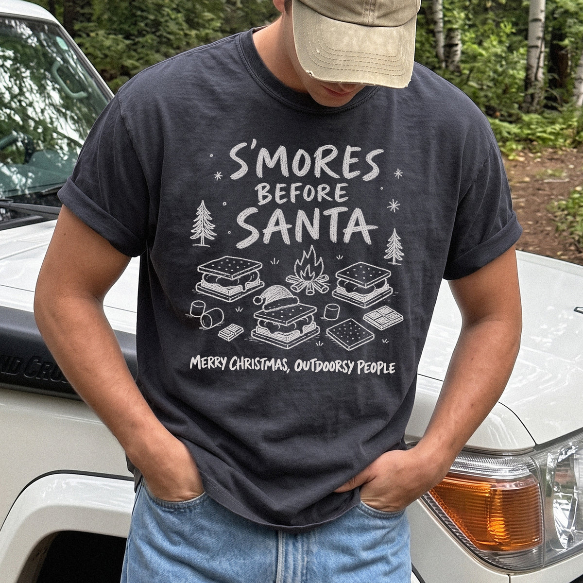 Man wearing a Graphite T-shirt printed with s’mores, a crackling campfire, marshmallows, chocolate pieces, pine trees, and a tiny Santa hat, doodle style