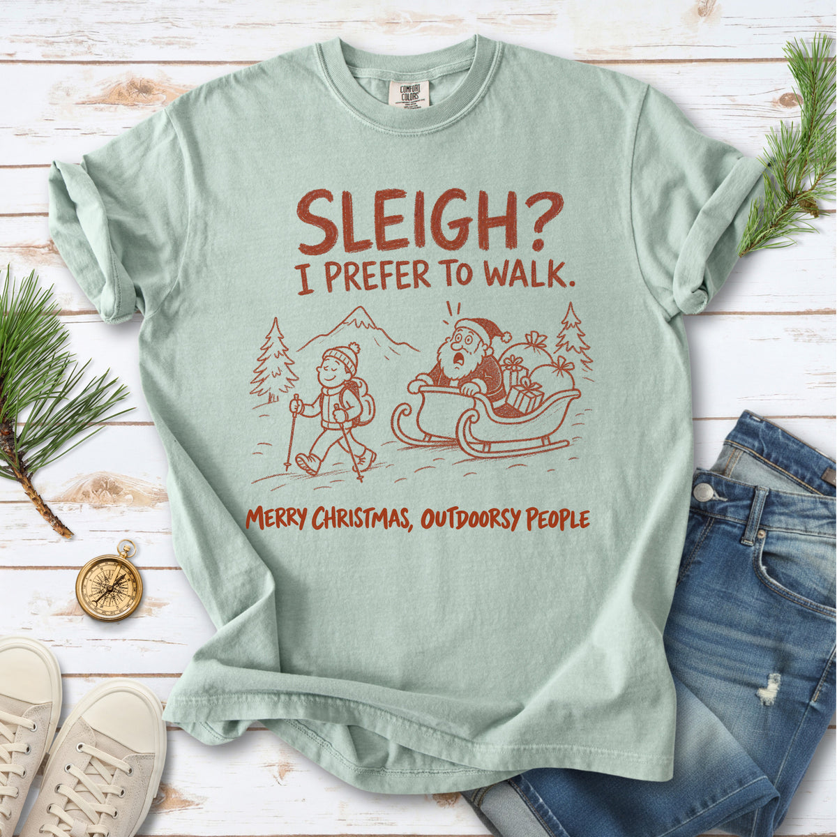 A hiker with trekking poles and a surprised Santa in his sleigh against a mountain backdrop, doodle line-art style design on a Bay T-shirt