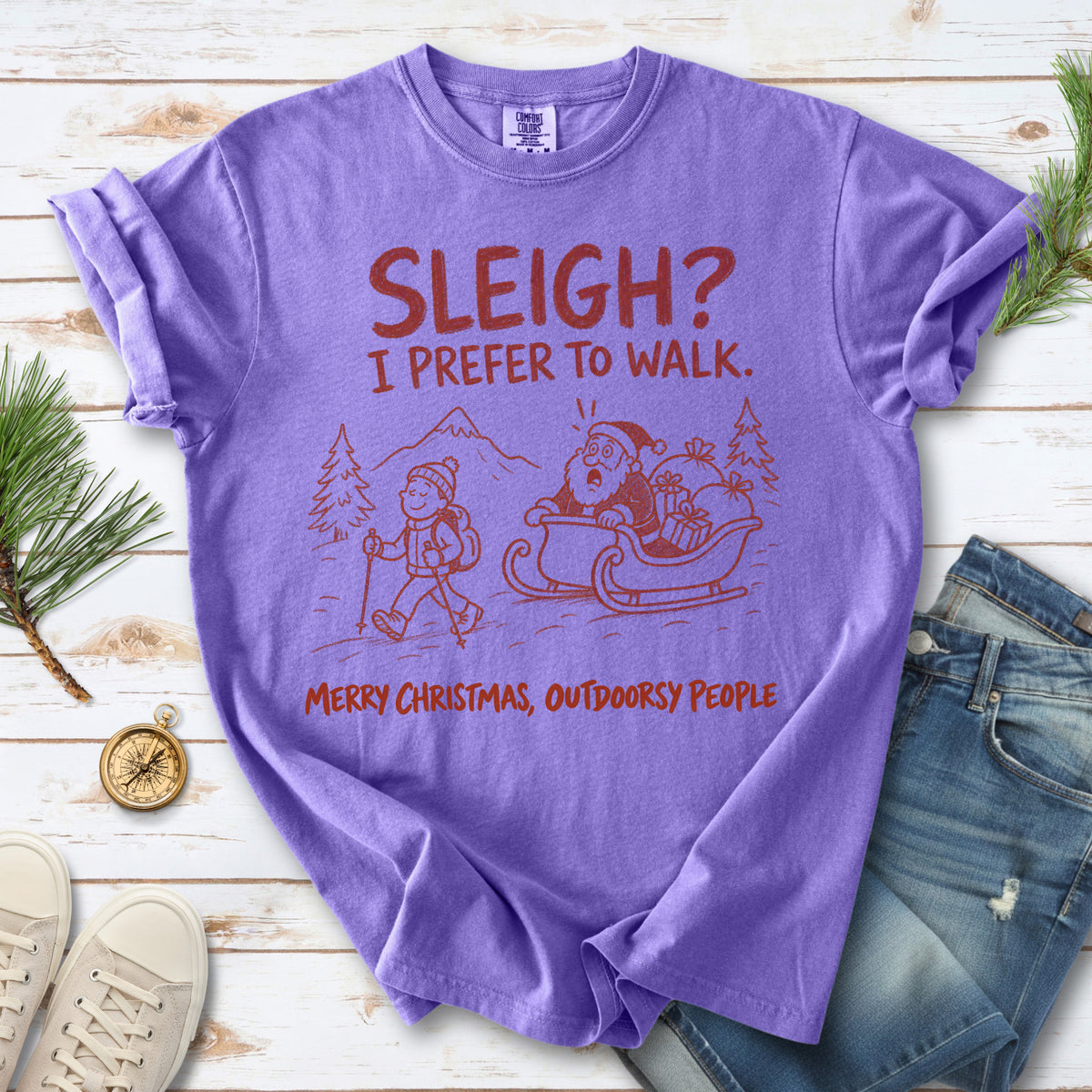 A hiker with trekking poles and a surprised Santa in his sleigh against a mountain backdrop, doodle line-art style design on a Violet T-shirt