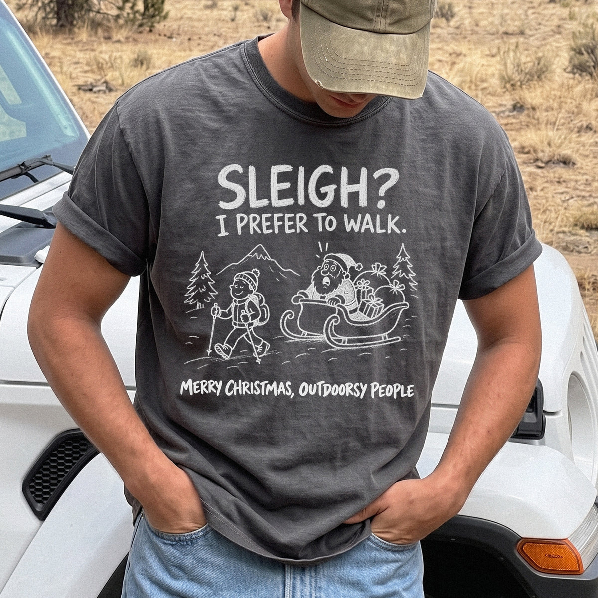 Man wearing a Pepper T-shirt printed with a hiker with trekking poles and a surprised Santa in his sleigh against a mountain backdrop, doodle line-art style