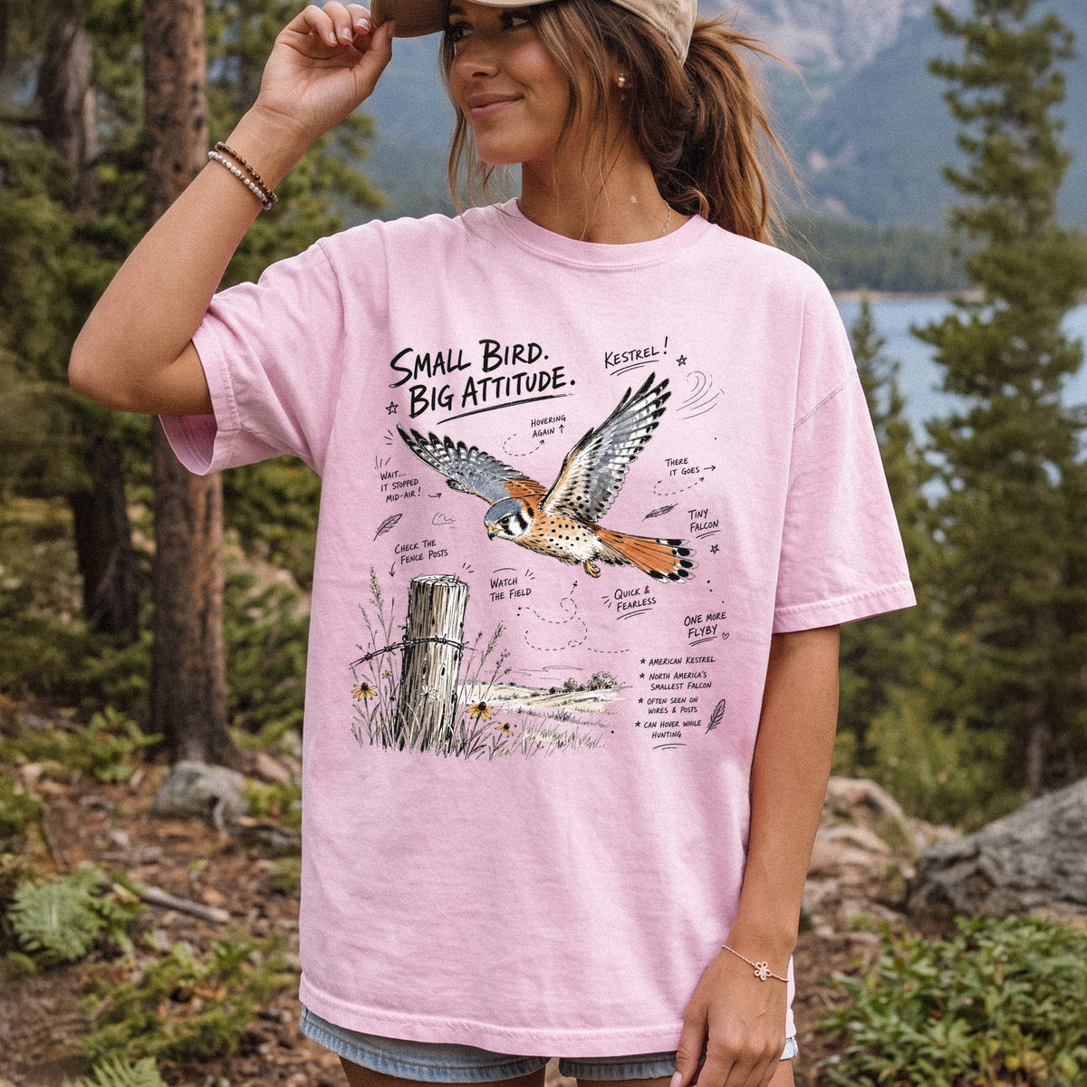 Small Bird, Big Attitude Comfort Colors Shirt – American Kestrel design of an American Kestrel illustrated in mid-flight above an open field, with fence-post details and field-note style callouts, printed on a Blossom T-shirt, worn by a woman.