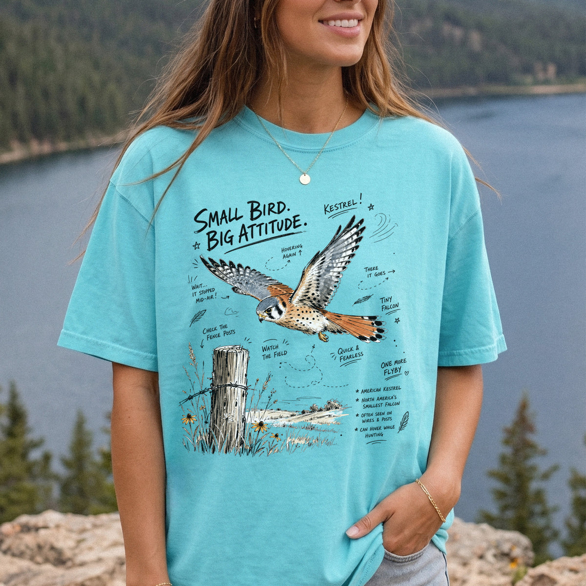 Small Bird, Big Attitude Comfort Colors Shirt – American Kestrel design of an American Kestrel illustrated in mid-flight above an open field, with fence-post details and field-note style callouts, printed on a Chalky Mint T-shirt, worn by a woman.