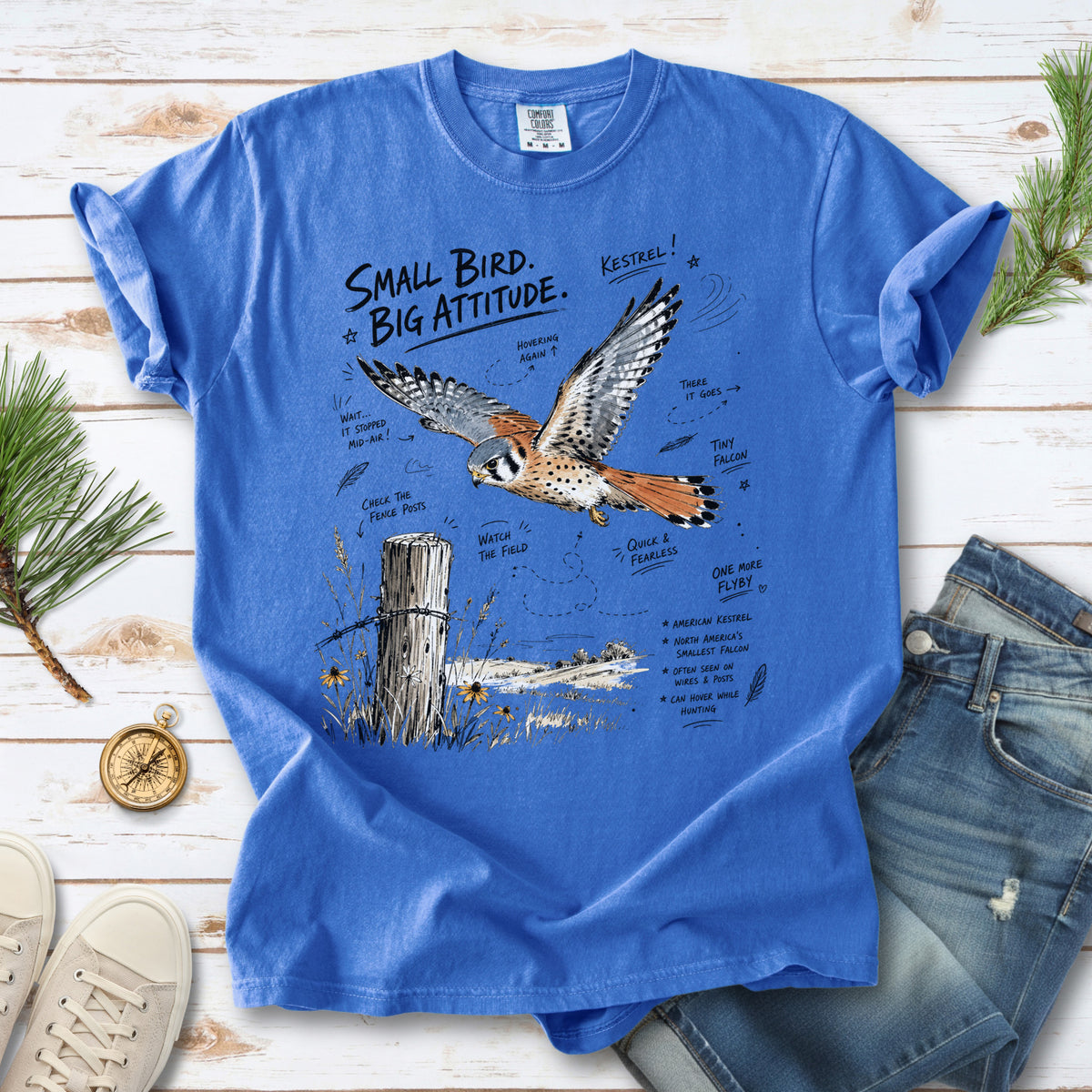 Small Bird, Big Attitude Comfort Colors Shirt – American Kestrel design of an American Kestrel illustrated in mid-flight above an open field, with fence-post details and field-note style callouts, printed on a Flo Blue T-shirt.