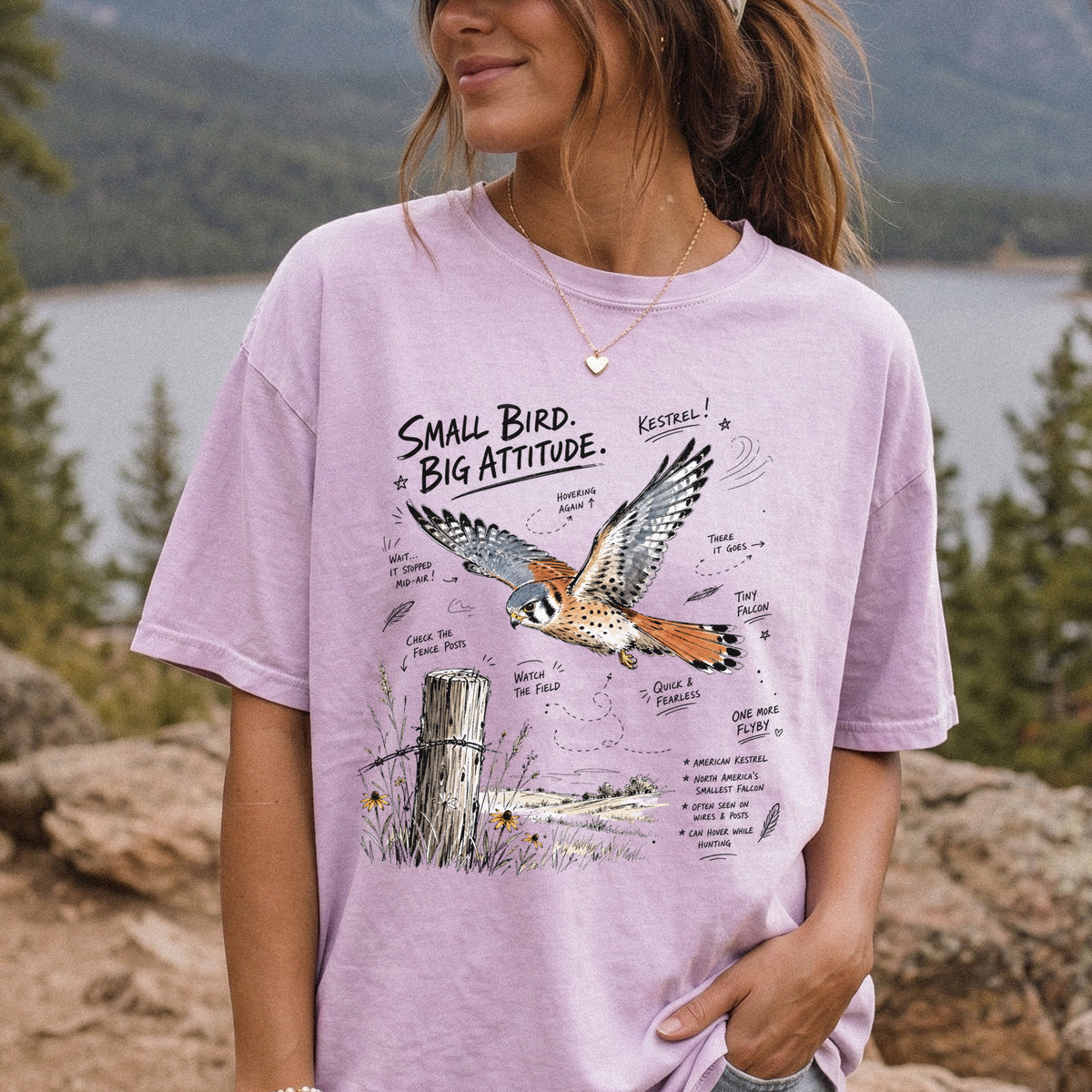 Small Bird, Big Attitude Comfort Colors Shirt – American Kestrel design of an American Kestrel illustrated in mid-flight above an open field, with fence-post details and field-note style callouts, printed on an Orchid T-shirt, worn by a woman.