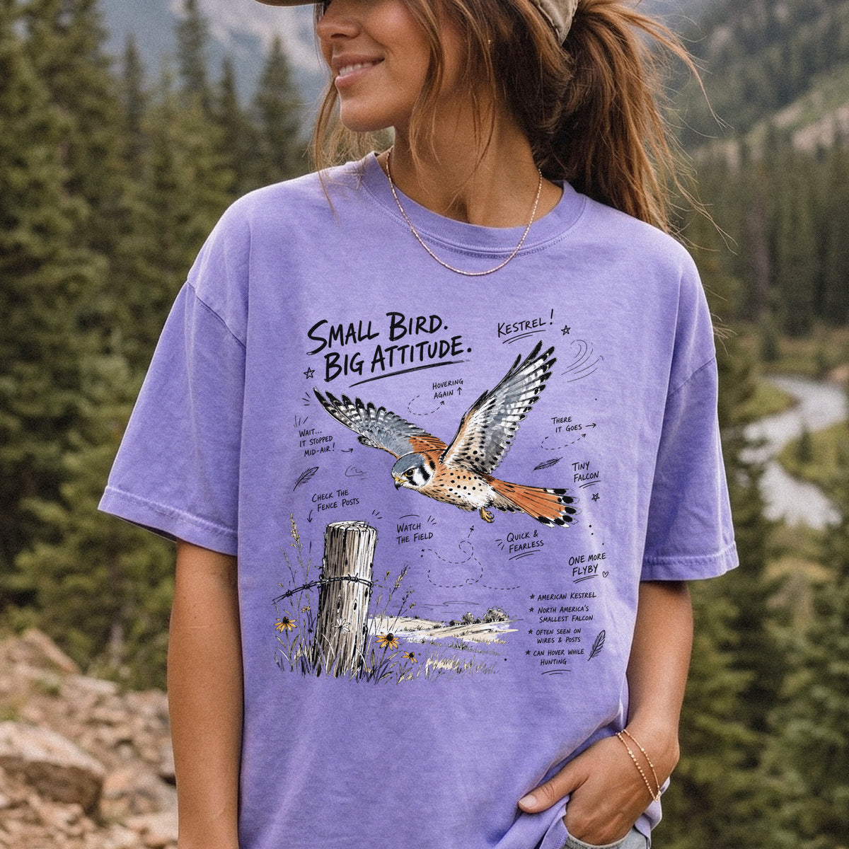 Small Bird, Big Attitude Comfort Colors Shirt – American Kestrel design of an American Kestrel illustrated in mid-flight above an open field, with fence-post details and field-note style callouts, printed on a Violet T-shirt, worn by a woman.