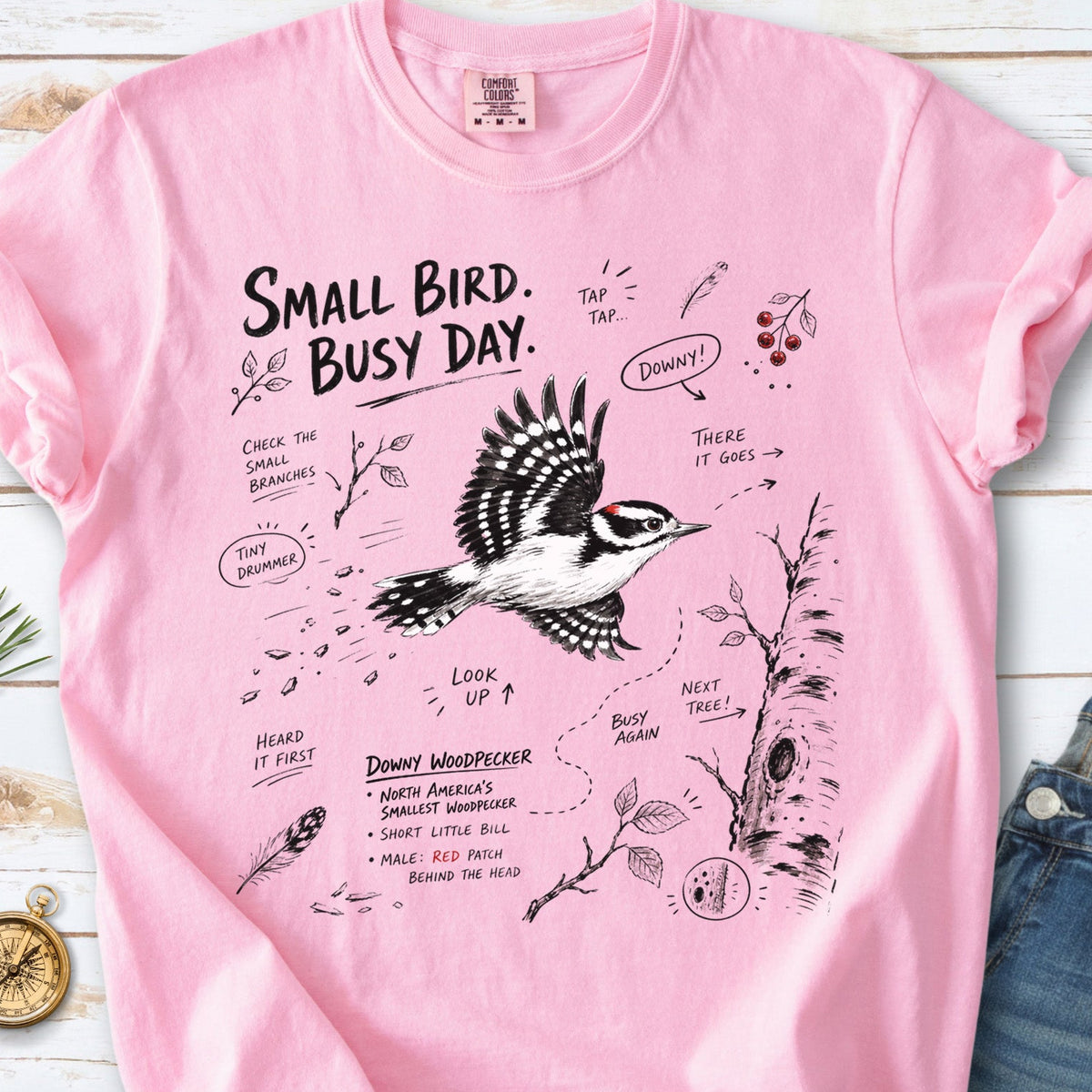 Small Bird Busy Day Comfort Colors Shirt – Downy Woodpecker design of a Downy Woodpecker illustrated in motion, along with sketch-style notes, branches, and tree-trunk details, printed on a Blossom T-shirt.