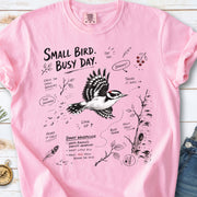 Small Bird Busy Day Comfort Colors Shirt – Downy Woodpecker design of a Downy Woodpecker illustrated in motion, along with sketch-style notes, branches, and tree-trunk details, printed on a Blossom T-shirt.