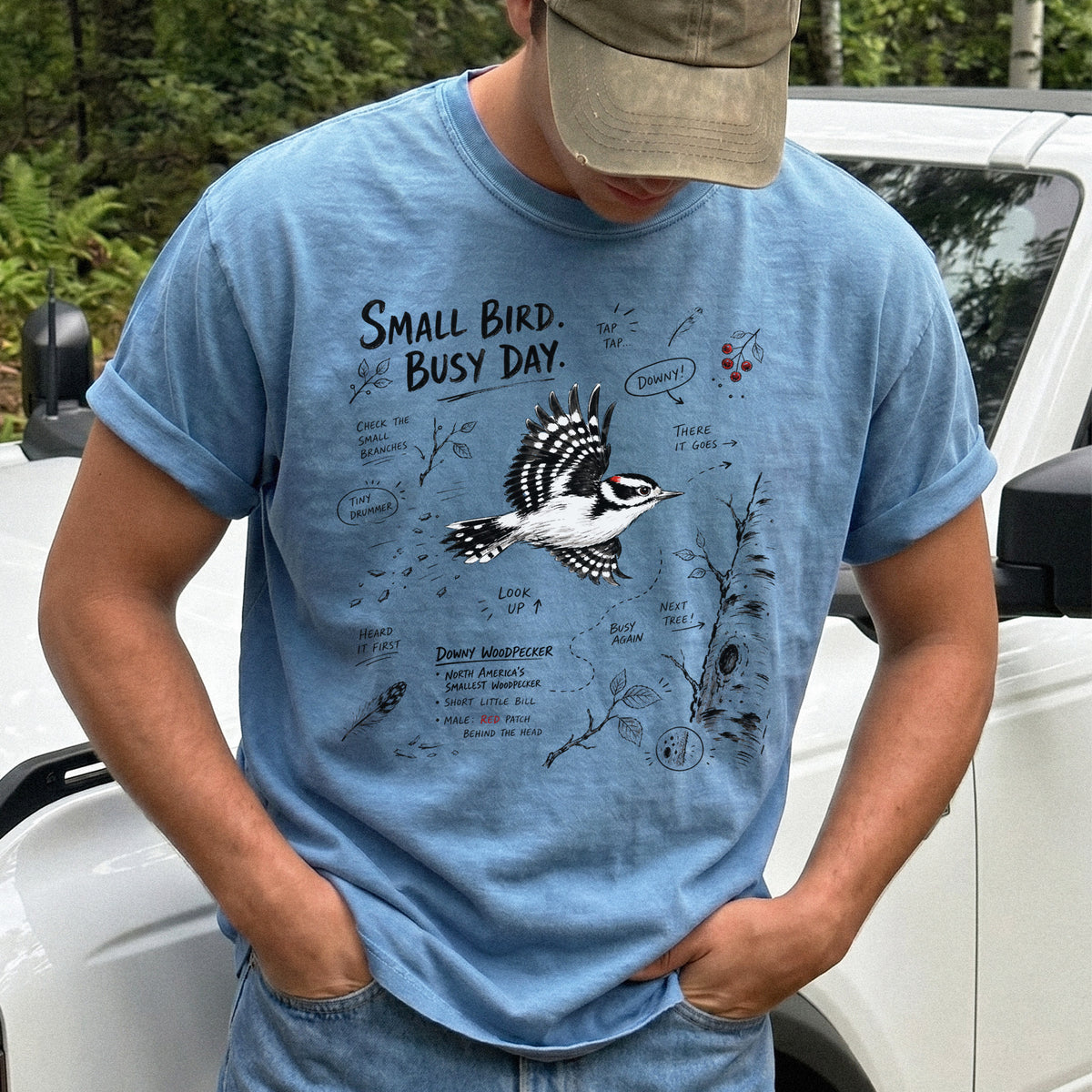 Small Bird Busy Day Comfort Colors Shirt – Downy Woodpecker design of a Downy Woodpecker illustrated in motion, along with sketch-style notes, branches, and tree-trunk details, printed on a Blue Jean T-shirt.