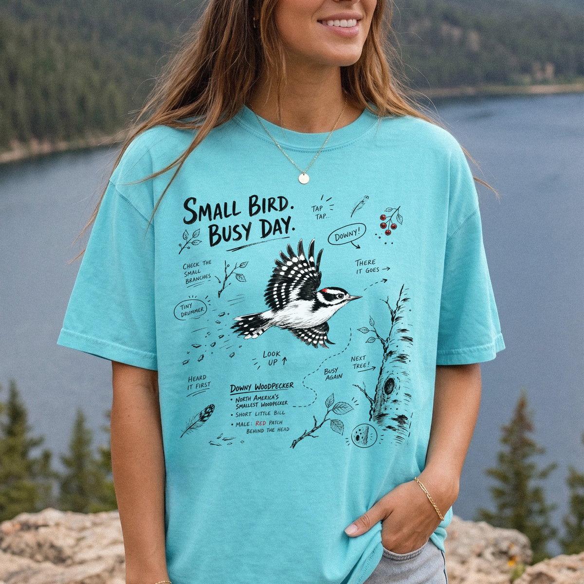 Small Bird Busy Day Comfort Colors Shirt – Downy Woodpecker design of a Downy Woodpecker illustrated in motion, along with sketch-style notes, branches, and tree-trunk details, printed on a Chalky Mint T-shirt, worn by a woman.