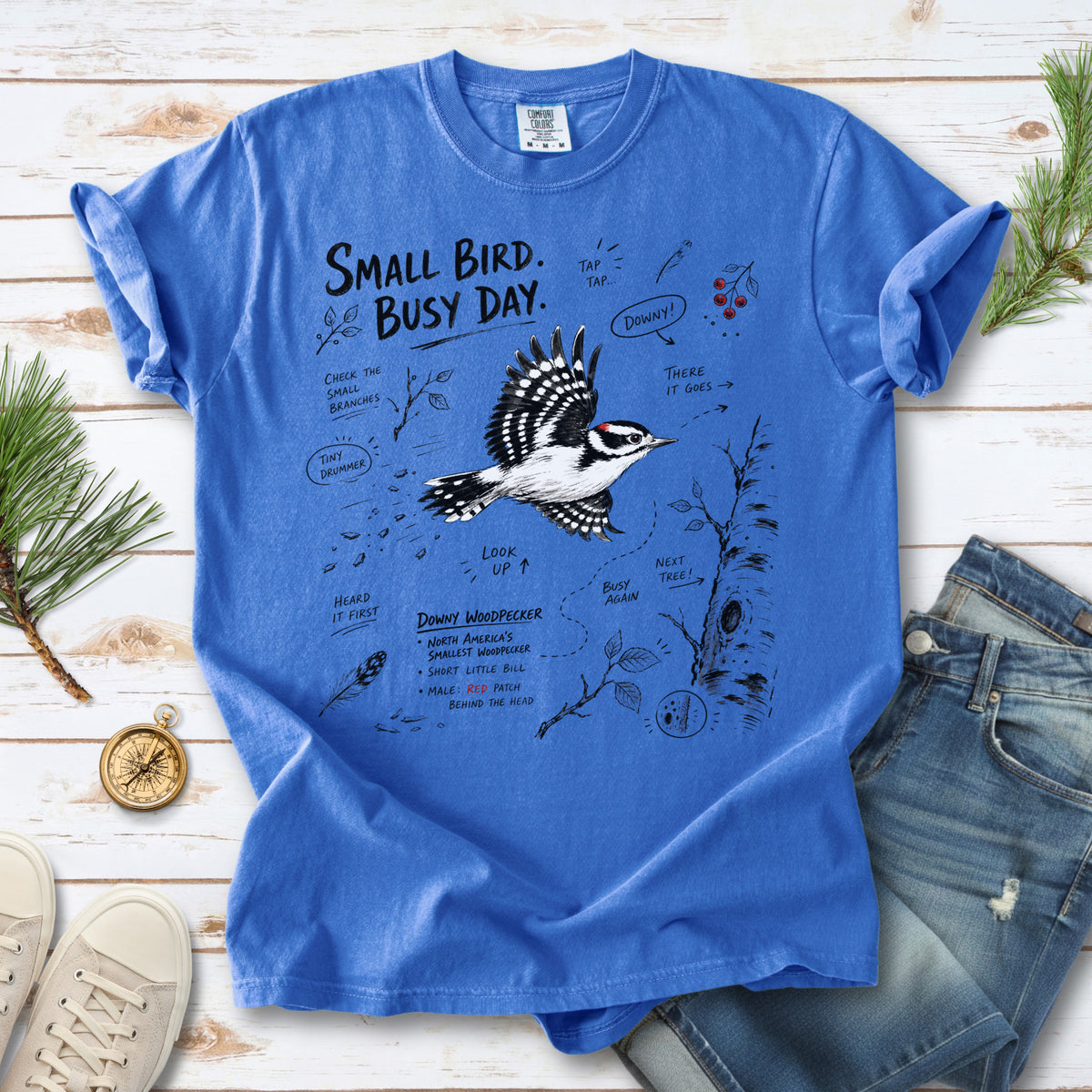 Small Bird Busy Day Comfort Colors Shirt – Downy Woodpecker design of a Downy Woodpecker illustrated in motion, along with sketch-style notes, branches, and tree-trunk details, printed on a Flo Blue T-shirt.