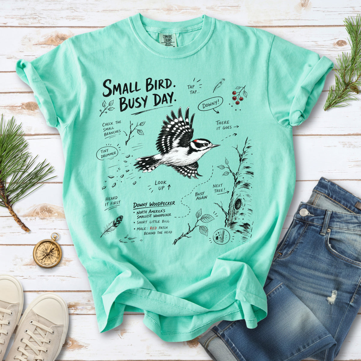 Small Bird Busy Day Comfort Colors Shirt – Downy Woodpecker design of a Downy Woodpecker illustrated in motion, along with sketch-style notes, branches, and tree-trunk details, printed on an Island Reef T-shirt.