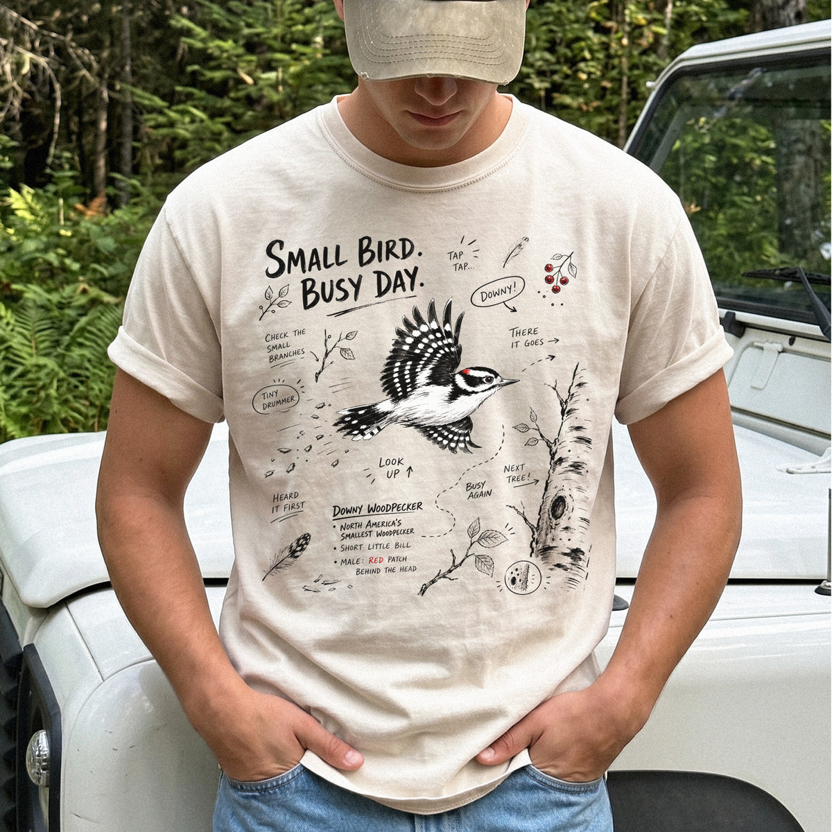 Small Bird Busy Day Comfort Colors Shirt – Downy Woodpecker design of a Downy Woodpecker illustrated in motion, along with sketch-style notes, branches, and tree-trunk details, printed on an Ivory T-shirt.