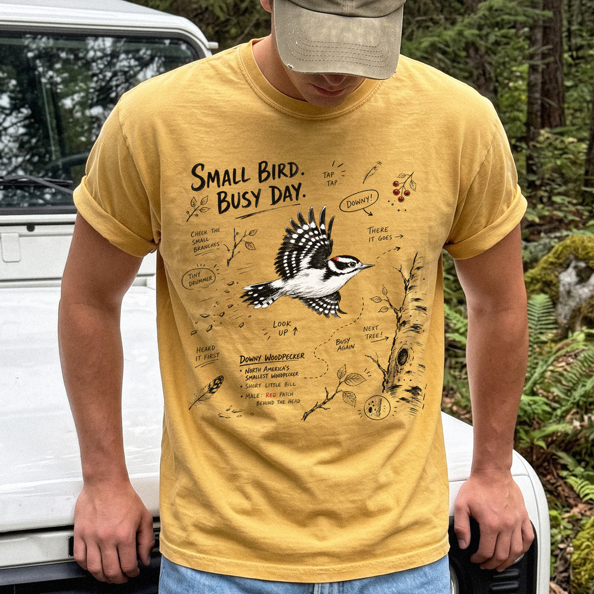 Small Bird Busy Day Comfort Colors Shirt – Downy Woodpecker design of a Downy Woodpecker illustrated in motion, along with sketch-style notes, branches, and tree-trunk details, printed on a Mustard T-shirt.