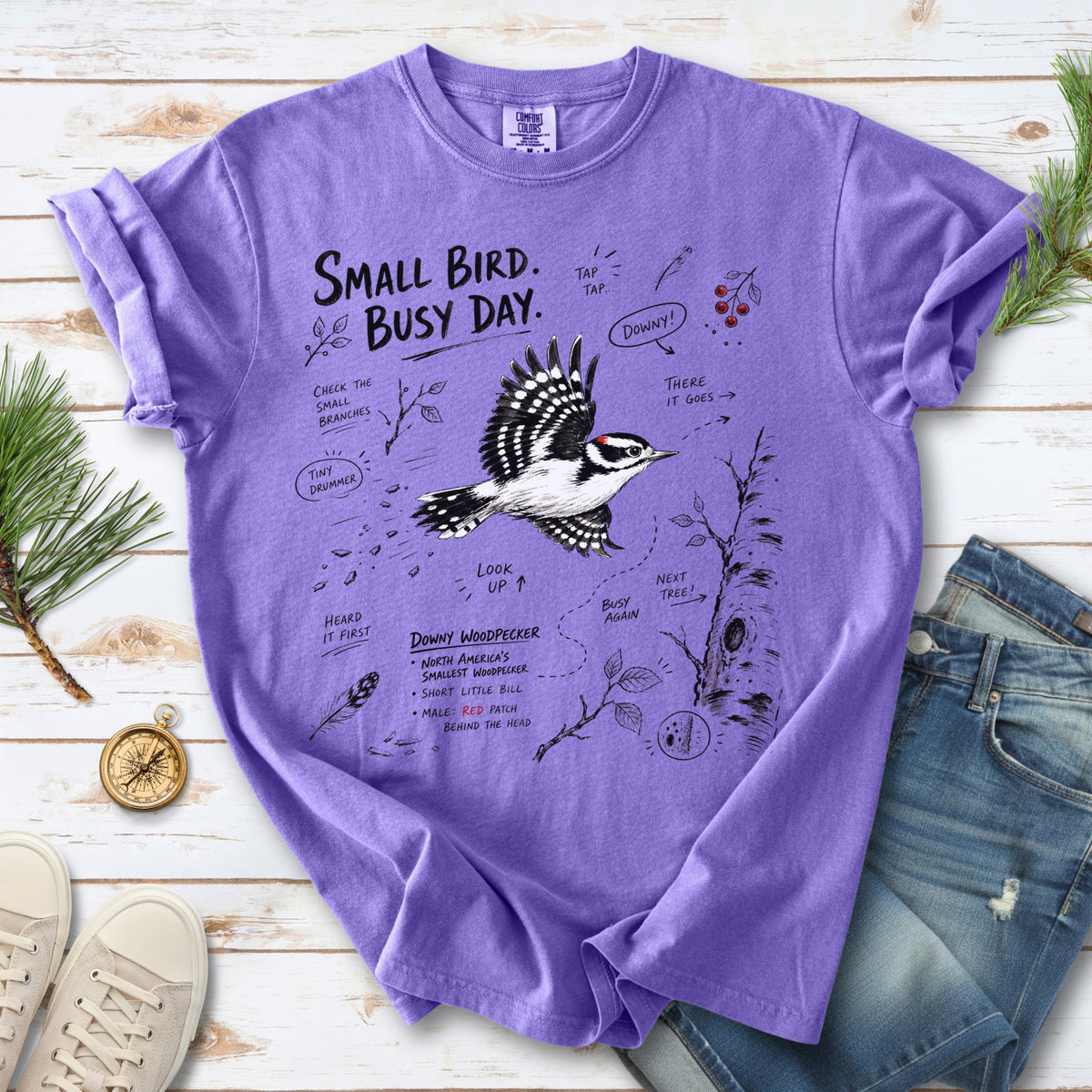 Small Bird Busy Day Comfort Colors Shirt – Downy Woodpecker design of a Downy Woodpecker illustrated in motion, along with sketch-style notes, branches, and tree-trunk details, printed on a Violet T-shirt.