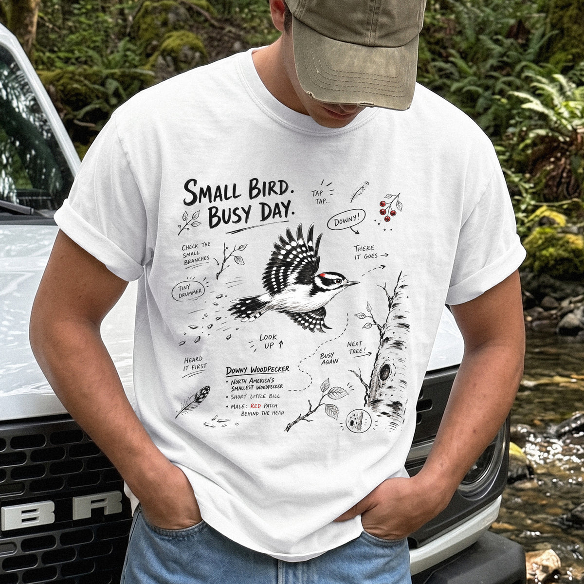 Small Bird Busy Day Comfort Colors Shirt – Downy Woodpecker design of a Downy Woodpecker illustrated in motion, along with sketch-style notes, branches, and tree-trunk details, printed on a White T-shirt.