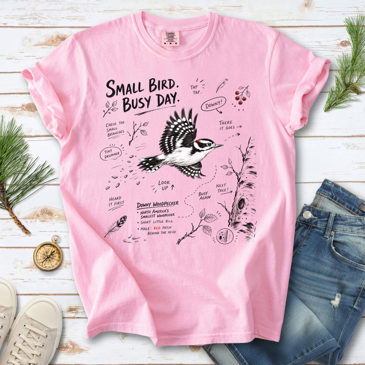 Small Bird Busy Day Comfort Colors Shirt – Downy Woodpecker design of a Downy Woodpecker illustrated in motion, along with sketch-style notes, branches, and tree-trunk details, printed on a Blossom T-shirt.