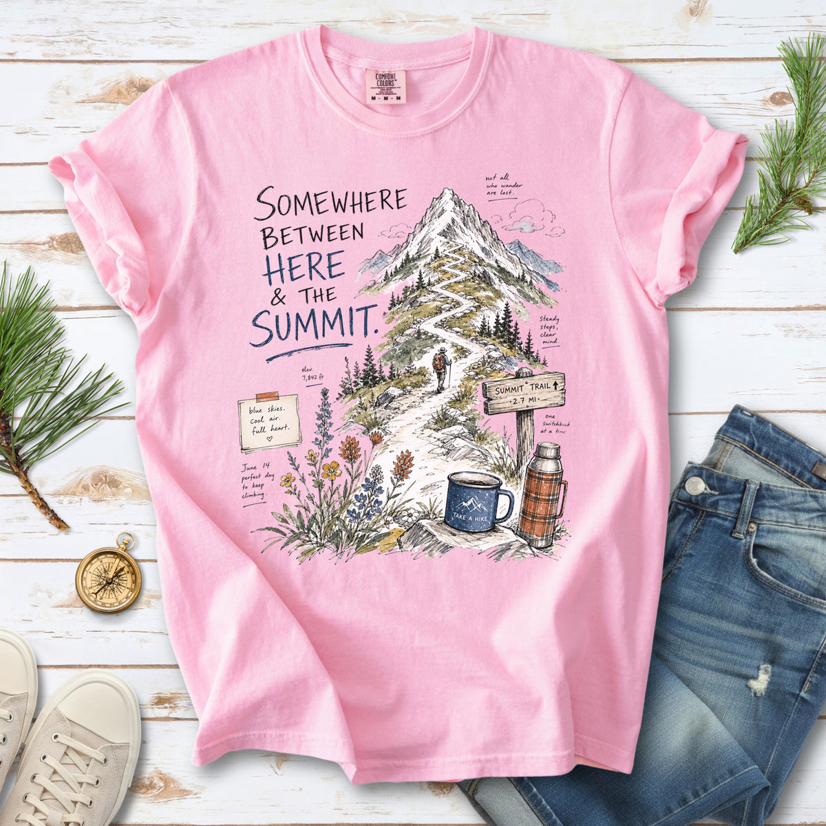 A hand-drawn mountain summit trail scene with wildflowers, a trail sign, a hiker, and a camp mug design on a Blossom T-shirt