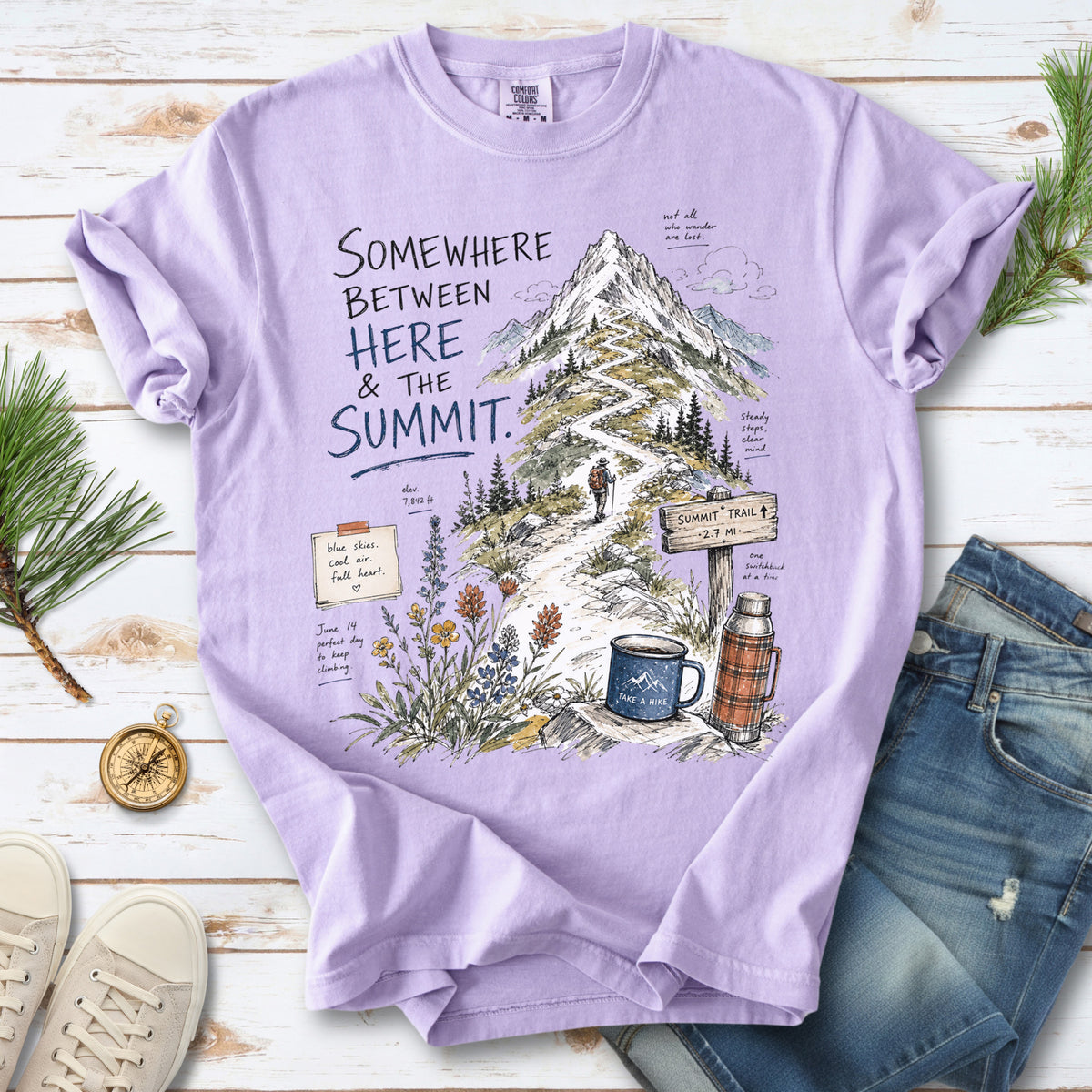 A hand-drawn mountain summit trail scene with wildflowers, a trail sign, a hiker, and a camp mug design on an Orchid T-shirt